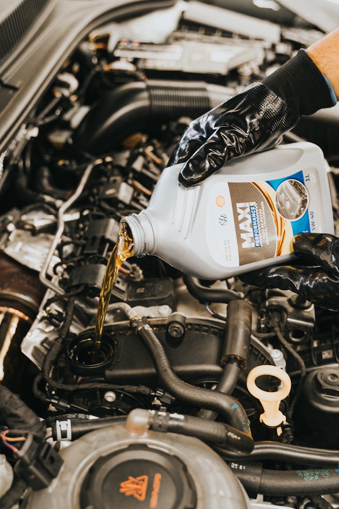 Home Close-up of mechanic pouring engine oil into car engine with gloved hands, showcasing automotive maintenance.